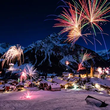 New Year 2025 Colorful fireworks over snowy alpine village at night with mountains in the background